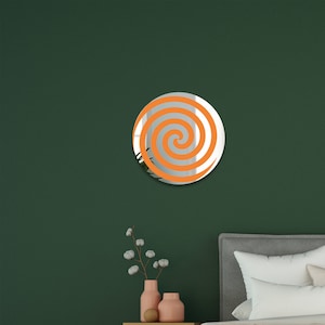 May include: A round mirror with a swirling orange design on a green wall. The mirror is hanging above a nightstand with two vases.