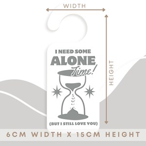 May include: A white door hanger with a grey hourglass and the text "I need some alone time! (But I still love you)". The hanger measures 6 cm wide by 15 cm tall.