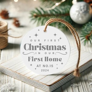May include: White round Christmas ornament with the text "Our First Christmas in Our First Home at No. 15 2024".