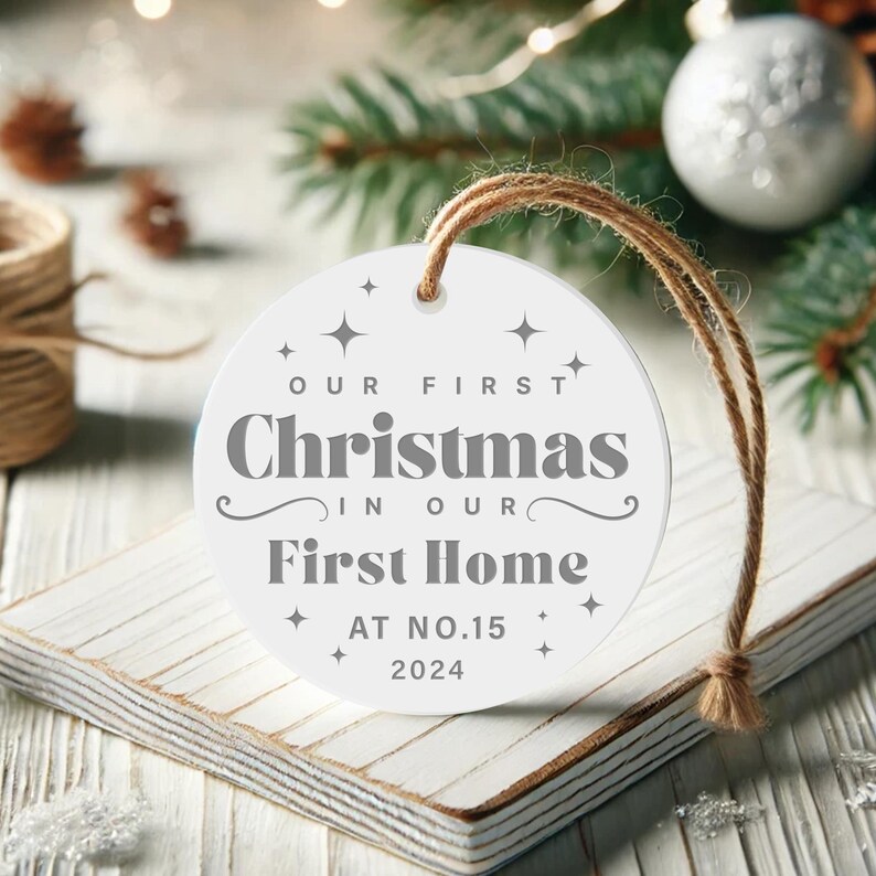 May include: White round Christmas ornament with the text "Our First Christmas in Our First Home at No. 15 2024".