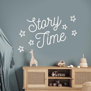 May include: A light blue wall with a white vinyl decal that says "Story Time" with stars around the text. A wooden dresser with a light wood finish and a woven rattan front is in the bottom of the image.