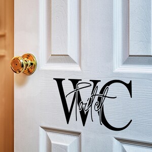 May include: A white door with a gold door knob and a black vinyl decal that says "WC Toilet" on it.