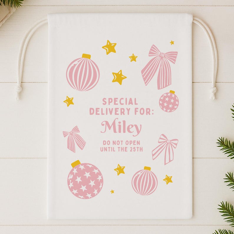 Puede incluir: Bolsa de regalo blanca con cord&oacute;n con adornos navide&ntilde;os rosas, lazos y estrellas doradas. El texto dice "SPECIAL DELIVERY FOR: Miley" y "DO NOT OPEN UNTIL THE 25TH". Una bolsa de regalo festiva.