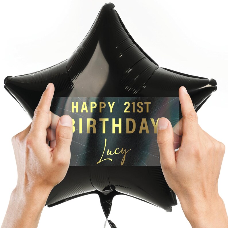 May include: A black star-shaped balloon with a gold foil sticker that says "Happy 21st Birthday Lucy".