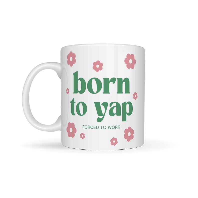 May include: White ceramic mug with a green design that says "born to yap" and "forced to work" in smaller text. The mug is decorated with pink flowers.