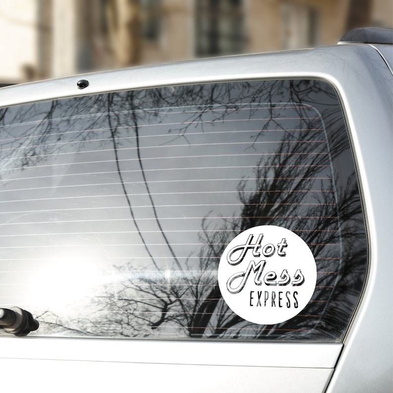 May include: A white circle sticker with black text that reads "Hot Mess Express" on a car window.
