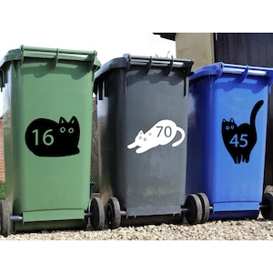 May include: Three green, black, and blue recycling bins with black and white cat stickers. The stickers have numbers on them: 16, 70, and 45.