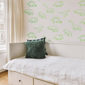 May include: A white daybed with a green throw pillow and a white wall with green dinosaur outlines.