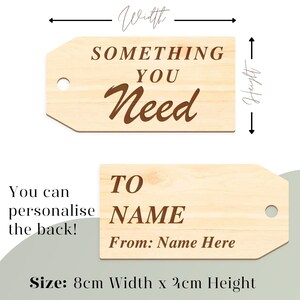 K&ouml;nnte beinhalten: H&ouml;lzerner Geschenkanh&auml;nger mit dem Text "Something You Need" in braunen Buchstaben. Die R&uuml;ckseite des Anh&auml;ngers tr&auml;gt den Text "To Name From: Name Here" und ist 8 cm breit und 4 cm hoch.