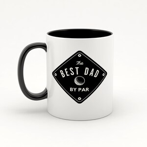 May include: White ceramic coffee mug with a black handle and black rim. The mug has a black and white graphic of a golf ball and the text "The Best Dad By Par".