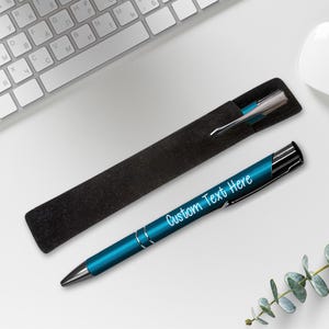 May include: A teal blue pen with a black and silver clip. The pen is engraved with the text "Custom Text Here". The pen is in a black velvet pen case.