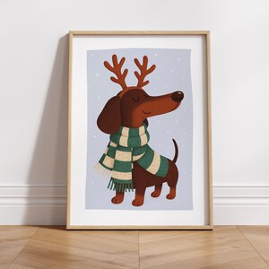 May include: A framed print featuring a cartoon dachshund wearing a green and white scarf and reindeer antlers. The dog is brown with a long snout and a happy expression. The background is a light blue with white dots.