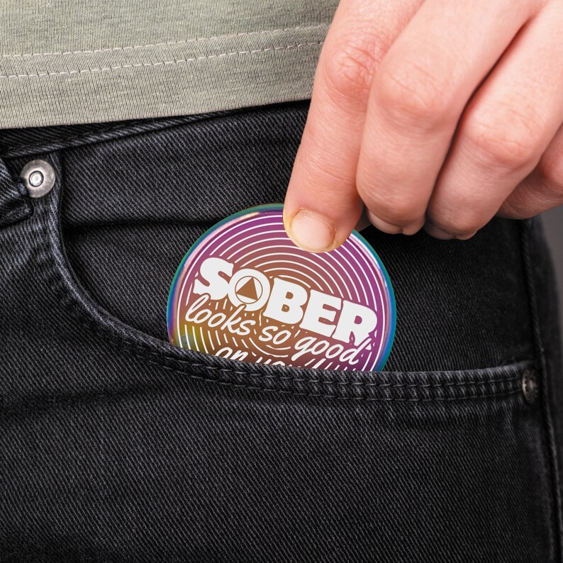 Pu&ograve; includere: Uno spillo rotondo arcobaleno iridescente con il testo "SOBER looks so good on you" in lettere bianche.