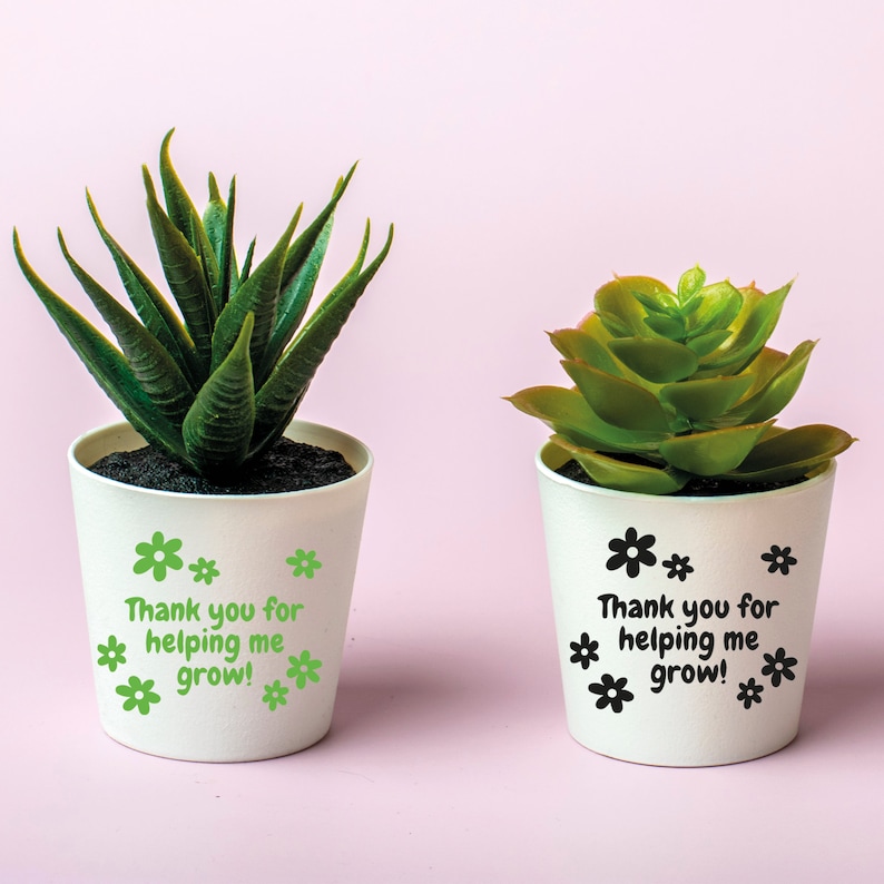 May include: Two white succulent pots with green plants. One pot has green flowers and the text "Thank you for helping me grow!" The other pot has black flowers and the same text.