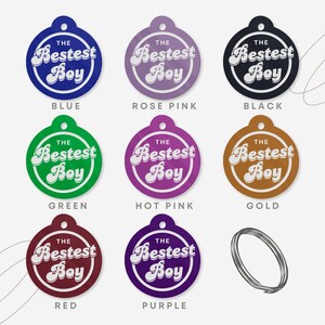 Puede incluir: Una colecci&oacute;n de etiquetas para mascotas de colores: azul, rosa, negro, verde, rosa intenso, dorado, rojo y morado. Cada etiqueta es redonda con el texto "The Bestest Boy" en un estilo retro. Tambi&eacute;n se incluye un llavero plateado.