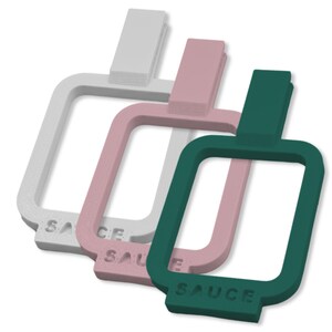 May include: Three silicone sauce bottle holders in white, pink, and green. Each holder has a rectangular shape with a small handle at the top and the word "SAUCE" printed on the bottom.
