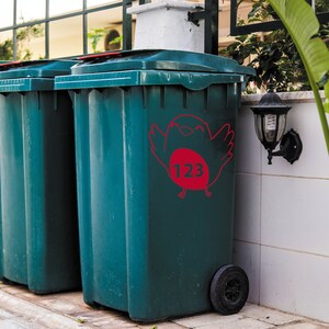 K&ouml;nnte beinhalten: Zwei gr&uuml;ne Recyclingbeh&auml;lter mit einem Vogelaufkleber auf einem Beh&auml;lter. Der Aufkleber hat die Nummer 123 in einem roten Kreis.