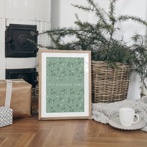 Puede incluir: Una impresi&oacute;n enmarcada con un fondo verde y un patr&oacute;n de mu&eacute;rdago blanco. El texto "It's Kissmas Time" est&aacute; impreso en blanco en la impresi&oacute;n.