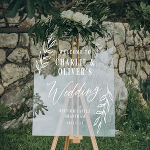 Pode incluir: Um sinal de casamento de acr&iacute;lico transparente com caligrafia branca que diz "Bem-vindos a Charlie & Oliver's Wedding" e inclui os detalhes "Belvoir Castle, Grantham, 10.11.23".