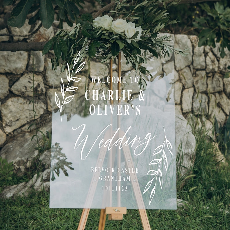 Pode incluir: Um sinal de casamento de acr&iacute;lico transparente com caligrafia branca que diz "Bem-vindos a Charlie & Oliver's Wedding" e inclui os detalhes "Belvoir Castle, Grantham, 10.11.23".