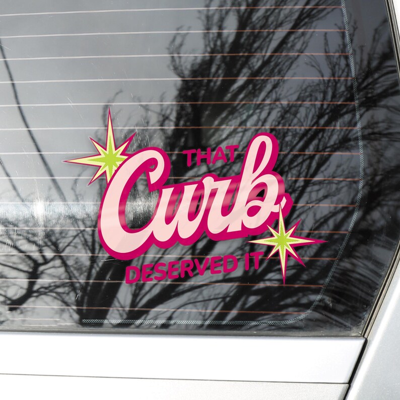 May include: A pink and white sticker with the words "That Curb Deserved It" in a retro font. The sticker has a starburst design in green and yellow. The sticker is on a car window.
