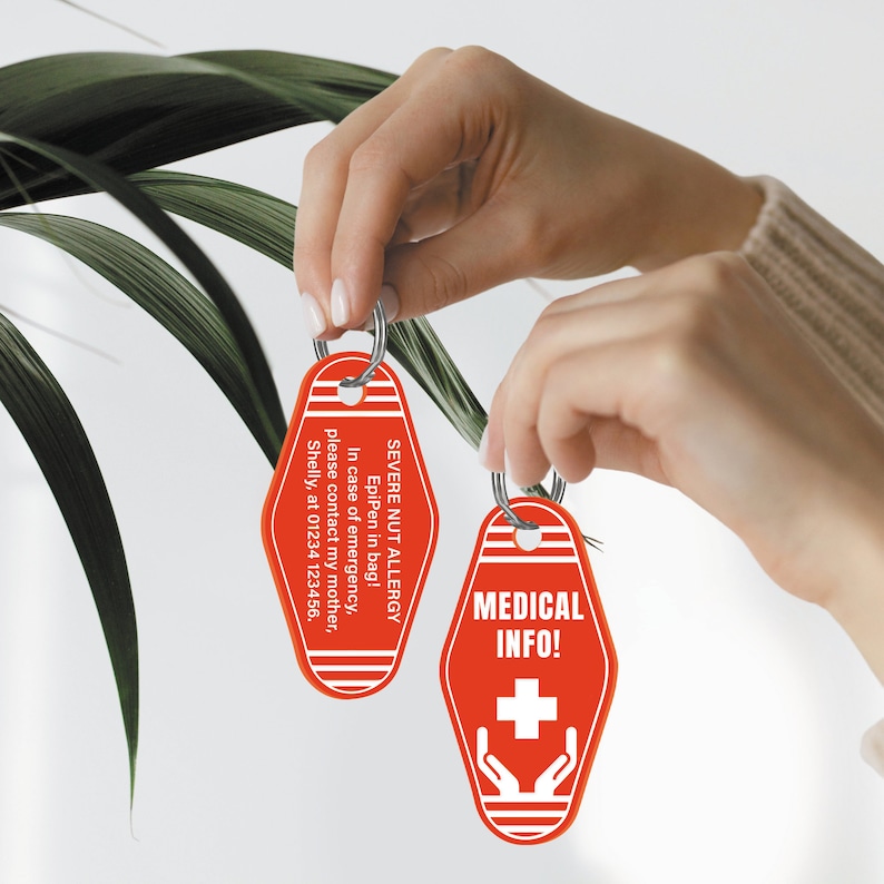 Pode incluir: Dois chaveiros de motel vermelhos com texto branco. Um chaveiro diz "SEVERE NUT ALLERGY EpiPen in bag! In case of emergency, please contact my mother, Shelly, at 01234 123456." O outro chaveiro diz "MEDICAL INFO!" com um sinal de mais branco e duas m&atilde;os segurando o sinal de mais.
