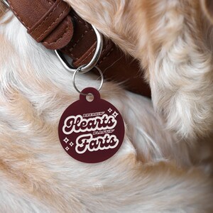 May include: A maroon dog tag with white text that reads "Breakin' Hearts Blastin' Farts".