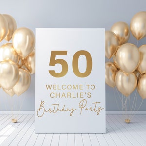 May include: A white sign with gold lettering that says "50 Welcome to Charlie's Birthday Party". The sign is surrounded by gold balloons.