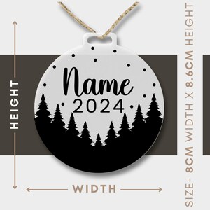 Może przedstawiać: Biała, okrągła ozdoba choinkowa z czarną sylwetką lasu i tekstem "Name 2024". Ozdoba ma 8,6 cm wysokości i 8 cm szerokości.