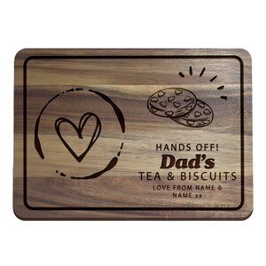 May include: A wooden cutting board with a heart and a cup of tea design. The text reads "Hands Off! Dad's Tea & Biscuits Love from NAME & NAME XX".