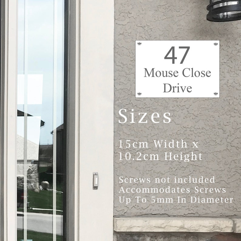 May include: White house number sign with black text, reading "47 Mouse Close Drive". The sign is 15 cm wide and 10.2 cm high.  The sign is mounted on a gray stucco wall.