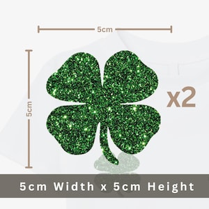 May include: Two green glitter shamrock appliques, each 5 cm wide and 5 cm high, are displayed on a white background. The image includes the text "x2" indicating the quantity. The shamrocks are a festive decoration.
