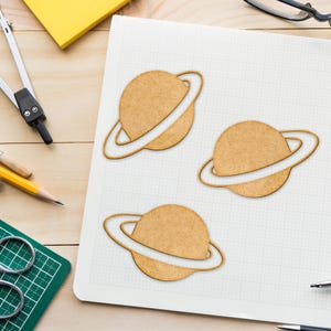 May include: Three brown paper planets with white rings on a white gridded paper background.