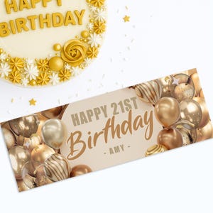 May include: A birthday cake with gold decorations and the words "Happy Birthday" in gold lettering. A banner with gold balloons and the words "Happy 21st Birthday - Amy -" is also present.