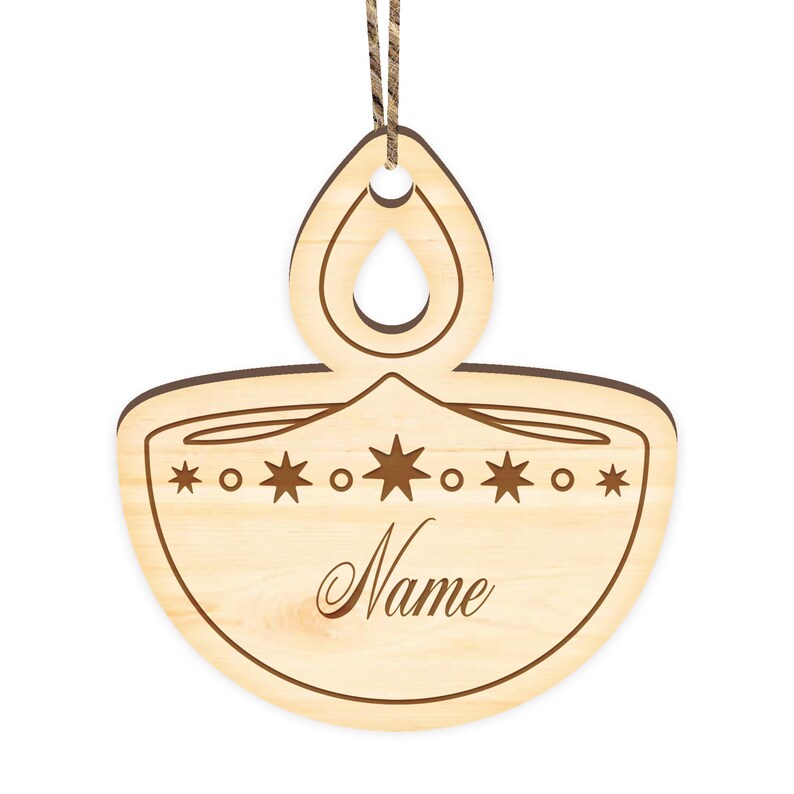 K&ouml;nnte beinhalten: Ein Holz-Anh&auml;nger in Form einer Diya, einer traditionellen indischen &Ouml;llampe, mit einer Schnur zum Aufh&auml;ngen. Der Anh&auml;nger ist mit Sternen verziert und das Wort "Name" ist auf der Vorderseite eingraviert.