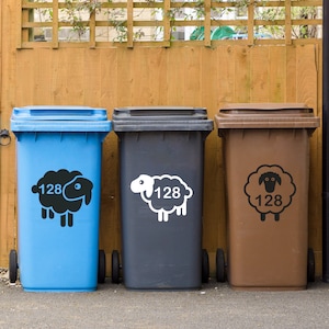 May include: Three blue, gray, and brown recycling bins with sheep stickers. Each bin has the number 128 on the sticker. The sheep on the blue bin is black, the sheep on the gray bin is white, and the sheep on the brown bin is black.