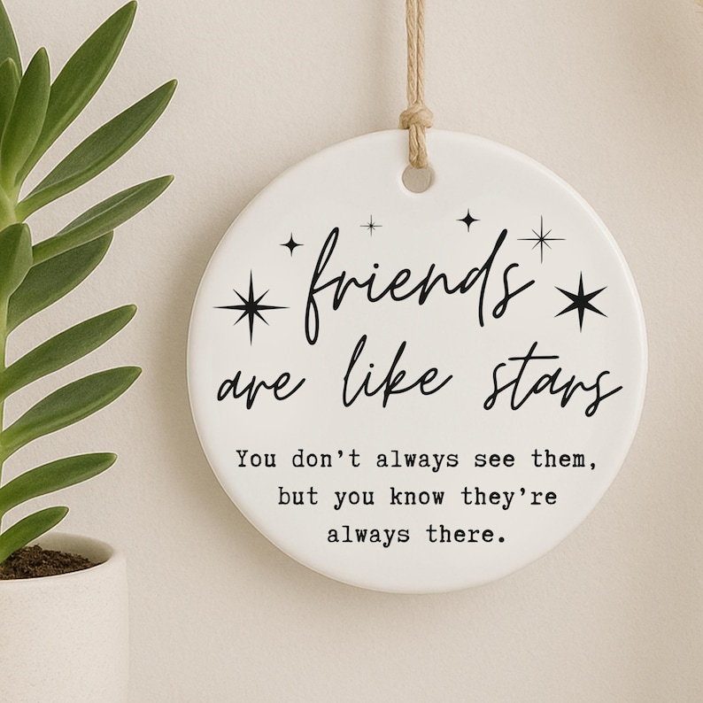 May include: A white ceramic disc with the text "friends are like stars" in black script. The disc has a string for hanging and is decorated with starburst designs. The quote continues: "You don't always see them, but you know they're always there."