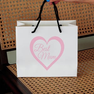 May include: White gift bag with black handles and a pink heart with the text "Best Mum" printed on it.