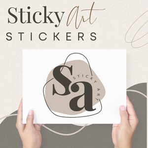 Puede incluir: Una tarjeta blanca con un logotipo marr&oacute;n y negro que dice "Sa" con las palabras "Sticky Art" escritas alrededor del logotipo. La tarjeta est&aacute; siendo sostenida por dos manos.