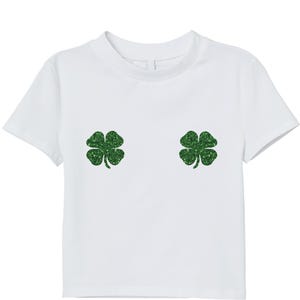 May include: White t-shirt with two glittery green four-leaf clover designs. The short-sleeved shirt has a crew neck and a simple, clean design, perfect for St. Patrick's Day or a touch of whimsy.