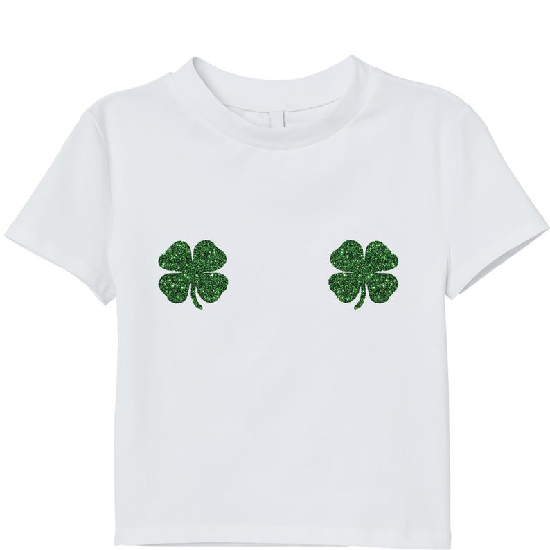 May include: White t-shirt with two glittery green four-leaf clover designs. The short-sleeved shirt has a crew neck and a simple, clean design, perfect for St. Patrick's Day or a touch of whimsy.