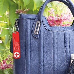 May include: Red keychain with a white plus sign and the text "Contact Information: 07877356473 0735261792".