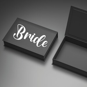 May include: A black box with the word "Bride" written in white cursive lettering. The box is open and empty.