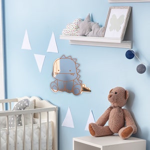 May include: A blue and rose gold dinosaur mirror for a nursery or child's room. The mirror is shaped like a cartoon dinosaur with a friendly face.