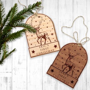 Op de afbeelding: Twee houten kerstversieringen in de vorm van sneeuwbollen met een hert erin. De versieringen zijn gepersonaliseerd met de tekst "Eric's First Christmas" en "Jane's First Christmas".