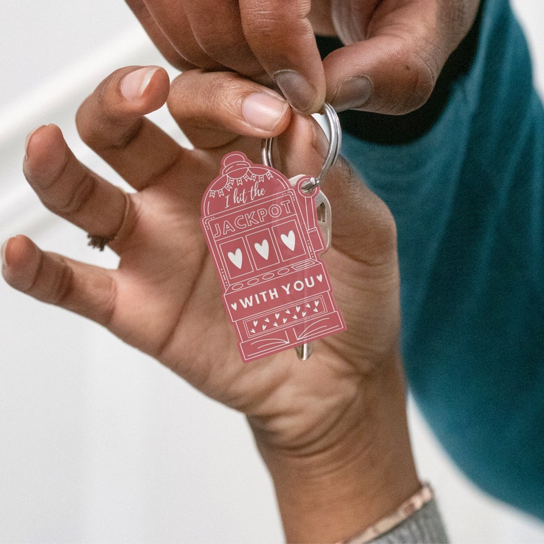 May include: A pink metal keychain shaped like a slot machine with the text "I hit the JACKPOT WITH YOU".