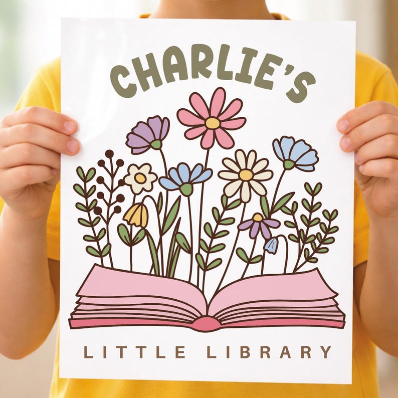 May include: A white print featuring the text "CHARLIE'S" above an open pink book with colorful flowers. The words "LITTLE LIBRARY" are below the book. The flowers include pink, purple, blue, yellow, and white blooms.