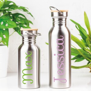 K&ouml;nnte beinhalten: Zwei Edelstahl-Wasserflaschen mit Bambusdeckeln. Die Flasche links tr&auml;gt den Namen "Max" in Gr&uuml;n auf der Seite. Die Flasche rechts tr&auml;gt den Namen "Jessica" in Pink auf der Seite.