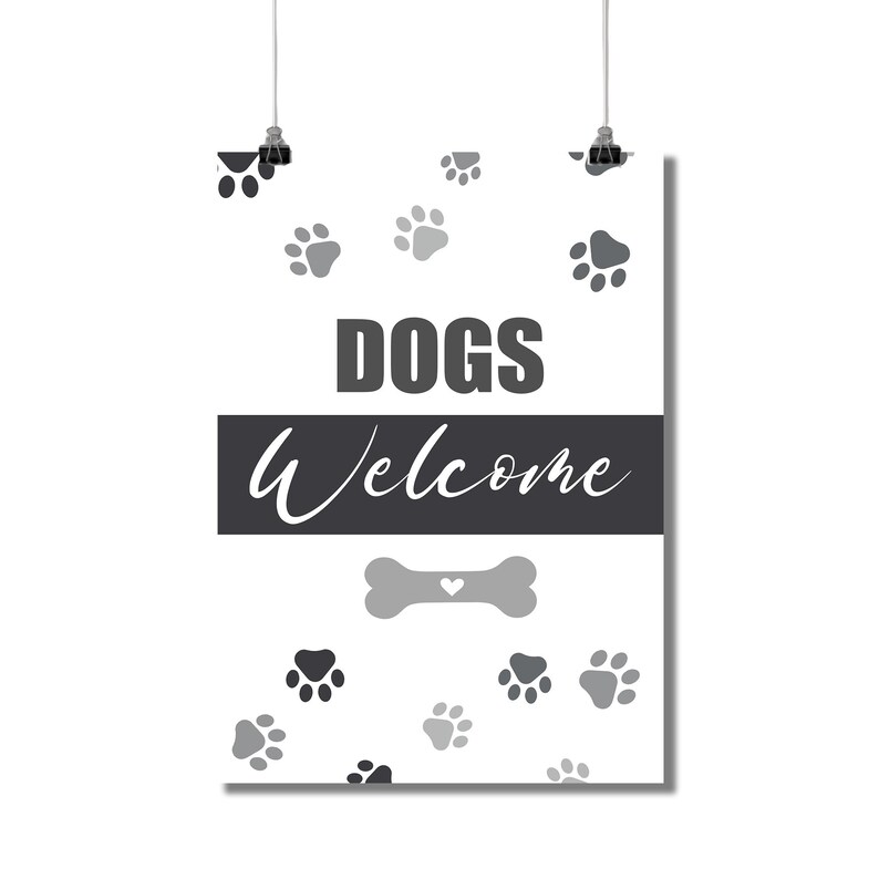 May include: A white poster with the words "DOGS Welcome" in gray and white. The poster has paw prints scattered across the background and a bone graphic. The poster is hanging from two black clips.