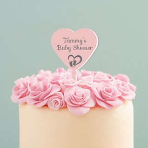 May include: Pink heart-shaped cake topper with the text "Tammy's Baby Shower" and a small footprint design.